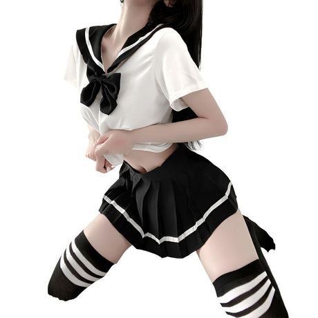 Medium shot front view of a model wearing a white Femzai sailor-inspired crop top with black accents and bow, paired with a black pleated skirt and striped thigh-high socks, set against a light bedroom backdrop, perfect for a trendy femboy look.