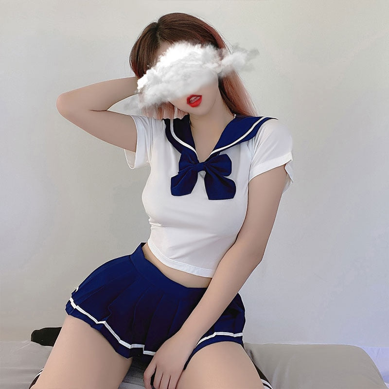 Medium shot of a model wearing the Femzai School Uniform set in white and blue; the ensemble includes a white crop top with a contrasting blue sailor collar and bow, paired with a deep blue pleated skirt with white trimming. The model poses against a neutral backdrop, her face obscured by a playful cloud graphic, highlighting a contemporary take on classic school attire.