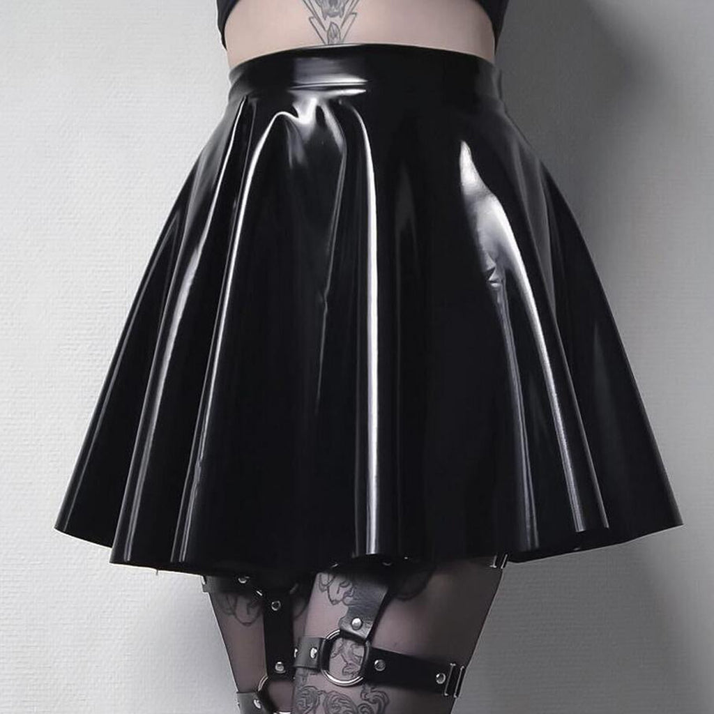 Close-up of a femzai-inspired black PVC pleated mini skirt. The high-gloss finish stands out, and the skirt is paired with intricately designed sheer tights. Black leather garters with metallic buckles add to the edgy look. A small tattoo is visible on the model's lower abdomen. The ensemble captures the essence of alternative and femboy fashion.