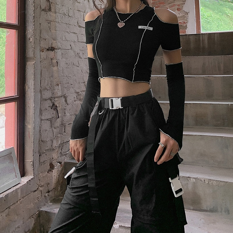 Medium shot side view of a model showcasing a black Femzai cut-out crop top and high-waisted pants with white accents against a rustic brick background, ideal for femboy clothing.