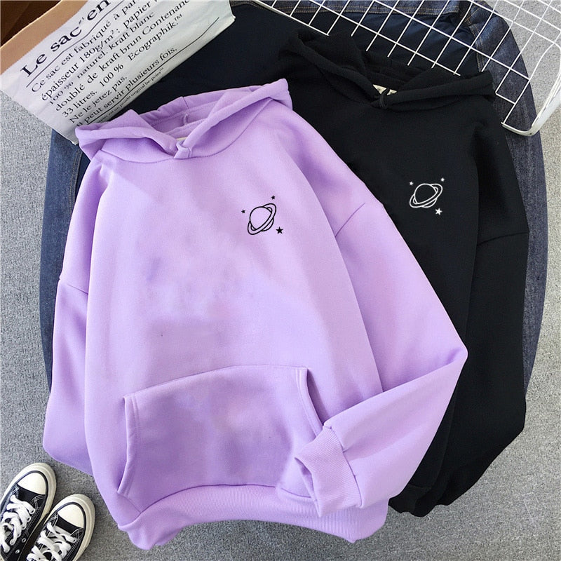 A flat-lay shot of a purple and black Saturn printed hoodie with a front pocket, displayed with casual sneakers, symbolizing femboy clothing style.