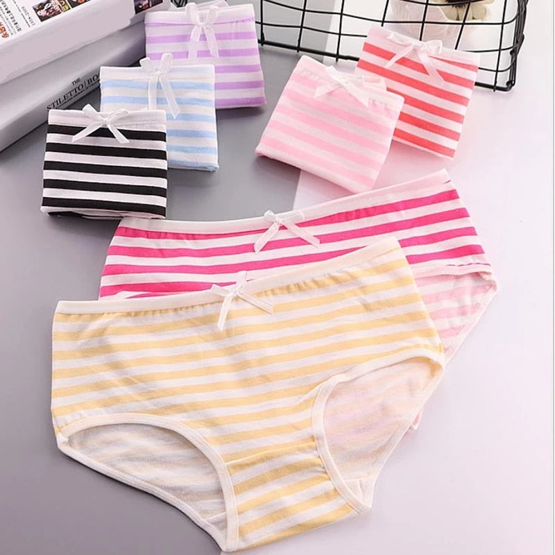 An assortment of striped panties in various colors, including pink, yellow, and black, neatly folded and presented against a white background. The shot captures the vibrant colors and the charming details like the white bows, emphasizing their suitability for femboy fashion.