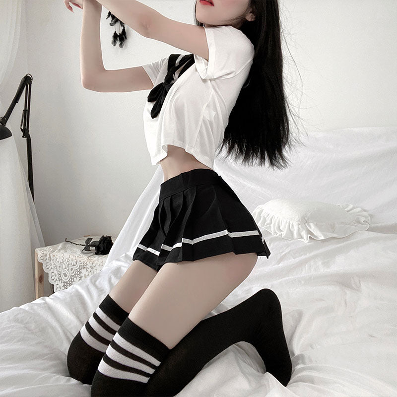 Medium shot side view of a model donning the Femzai School Uniform set; featuring a white crop top with black sailor collar and ribbon details, combined with a black pleated skirt with white trim, and matching striped thigh-high socks, presented against a calm bedroom setting, epitomizing a modern school-themed attire.