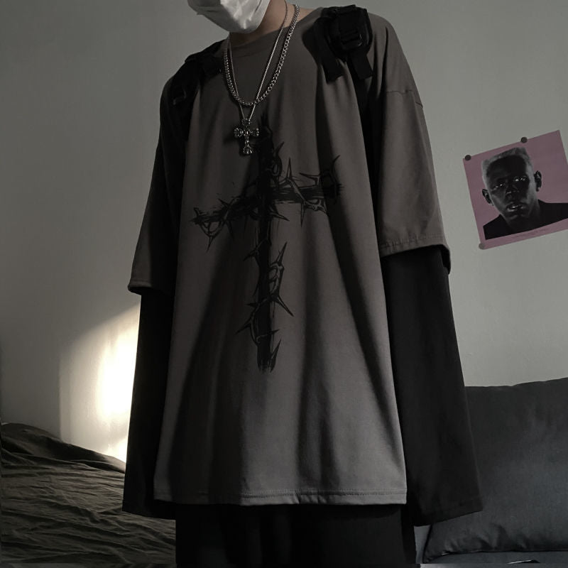 A low-light shot with a side view of a person donning a cross double-sleeve long sleeve top, a part of femboy clothing. The angle emphasizes the unique sleeve design and the graphic on the shirt, capturing the moody ambiance of the room.