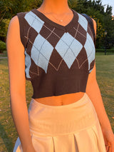 Medium shot front view of a model in a park setting wearing a brown and light blue Femzai Gridded V-neck Vest, paired with a soft cream-colored skirt during golden hour, capturing a serene and stylish outdoor vibe.