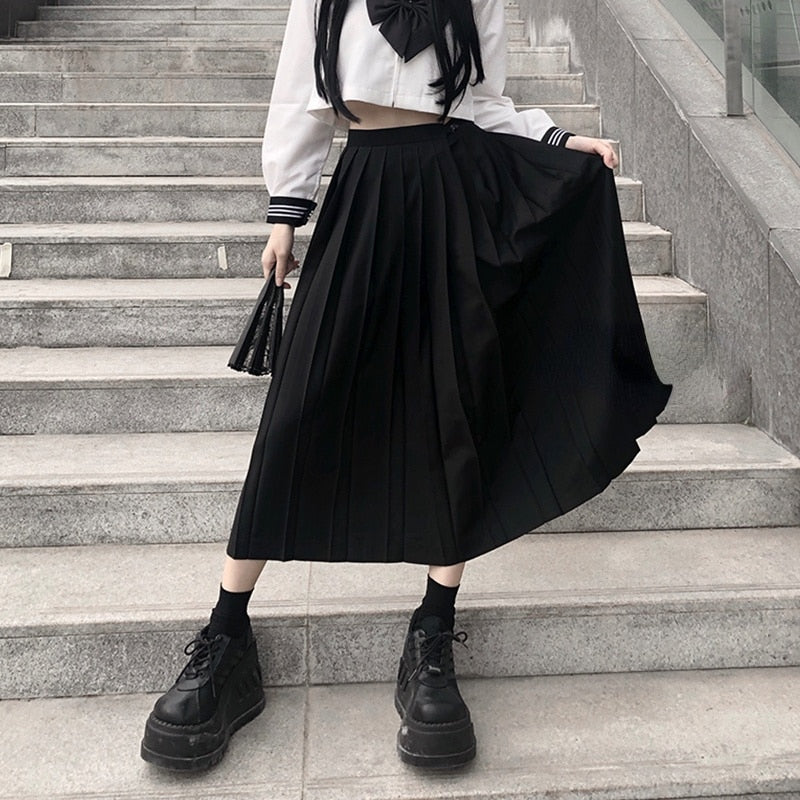 A person is captured mid-twirl on a staircase, wearing a long black pleated skirt with a white top, black ankle socks, and robust black platform shoes. The dynamic shot, taken from a low angle, emphasizes the movement of the skirt and contributes to the femboy fashion aesthetic.
