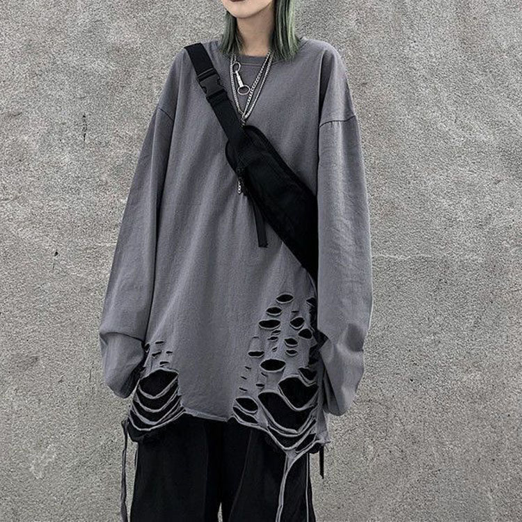 Medium shot front view of a gray Femzai oversized pullover with distinctive hem cut-outs paired with black pants, accentuated by a black sling bag and a silver necklace, showcasing a versatile and minimalist street style, ideal for femboy fashion trends.