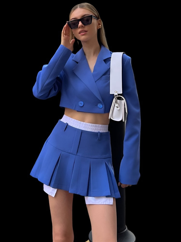 Elegant model donning a Femzai blue blazer suit skirt ensemble, emphasizing femboy attire trends, accessorized with sunglasses and a chic white sling bag against an urban backdrop.