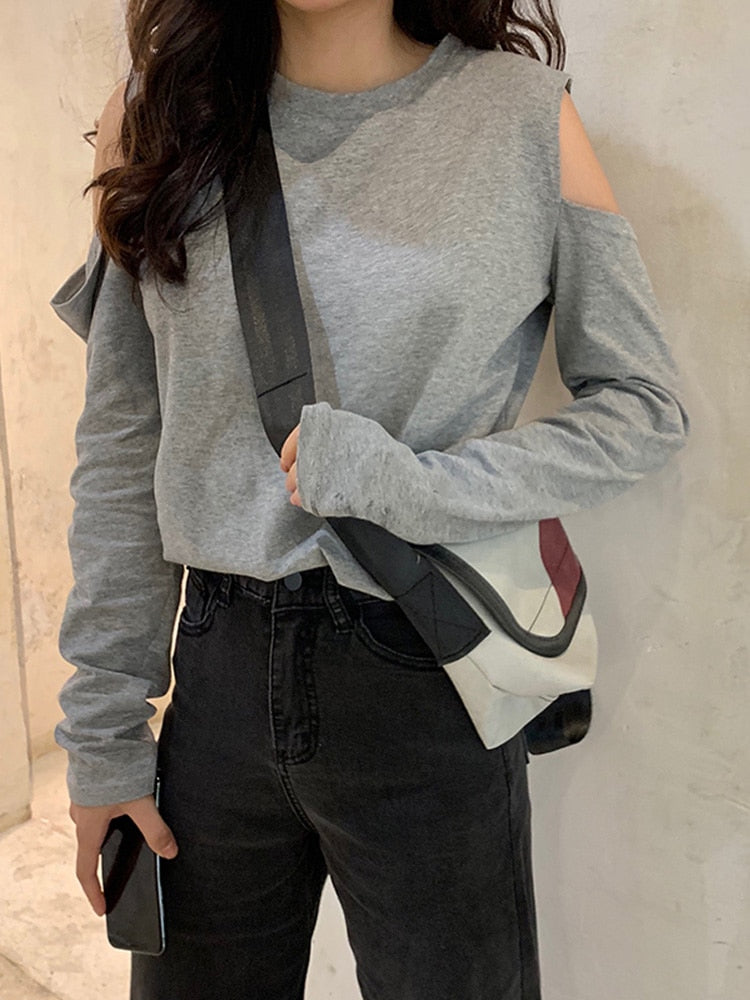 Close-up shot showcasing a model in a grey Femzai cold-shoulder sweatshirt with unique sleeve designs, paired with black high-waisted jeans and a trendy shoulder bag, against a light-colored background, ideal for stylish winter wear.