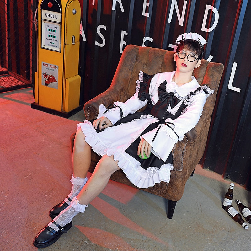 Image Description: Femzai's black and white maid dress product photo showcasing a close-up view. The model, wearing glasses and a coordinating maid headband, sits elegantly on a vintage brown chair. A nostalgic "SHELL" gasoline pump and red curtains with "TREND CASES" text provide a contrasting background.