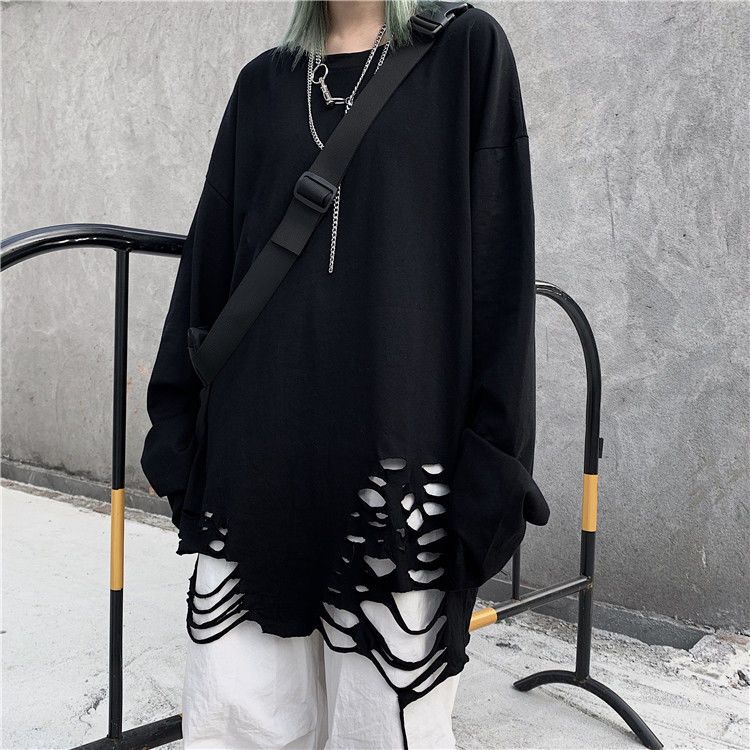 Medium shot side angle view displaying a black Femzai oversized sweatshirt with artistic cut-out patterns on the hem, complemented by a crossbody bag and silver chain necklace, set against an urban backdrop, embodying a unisex streetwear vibe suitable for a femboy wardrobe.