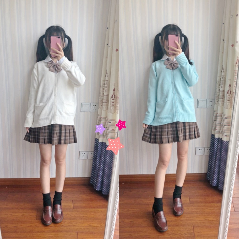 Front view of a model showcasing Femzai's femboy clothing, wearing a white JK sweater over a brown plaid skirt with a coordinating bow tie. The casual pose and mirror selfie add a personal touch to the outfit presentation.