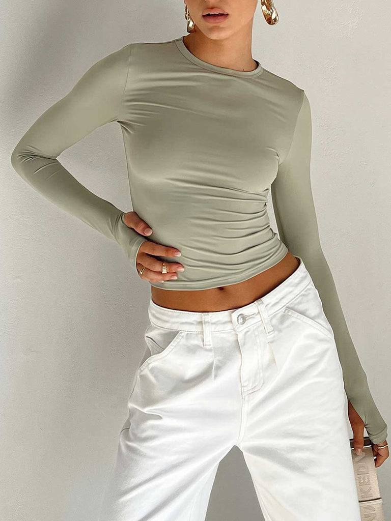 Medium shot angled view of a model wearing a sage green Femzai long-sleeve ruched top complemented with high-waisted white jeans, highlighting a subtle yet trendy style.