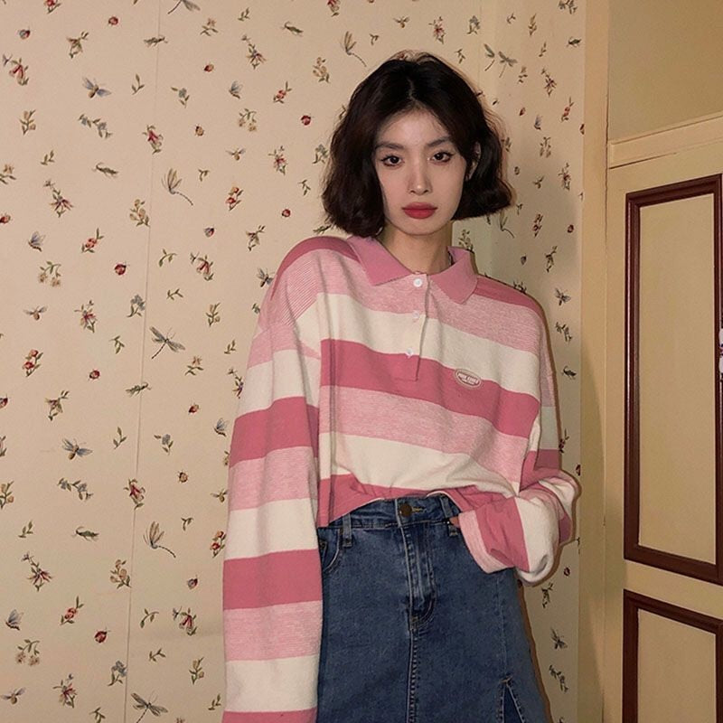 Close-up front view of Striped Collared Longsleeve in pink and white. Model is against a light beige wall with small floral designs, focusing on the top half of the shirt and detailing.
