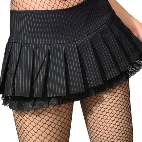 Close-up front view of our black Lightly Striped Pleated Mini Skirt worn by a model in fishnet stockings against a clean white background, showcasing intricate details.