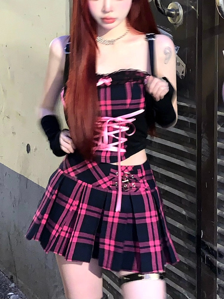 A frontal shot of the same femboy, gracefully standing with arms aloft, emphasizing the lace-up details of their black and pink plaid top. The look is complemented with a matching mini skirt and edgy black thigh bands, encapsulating the iconic femboy style.