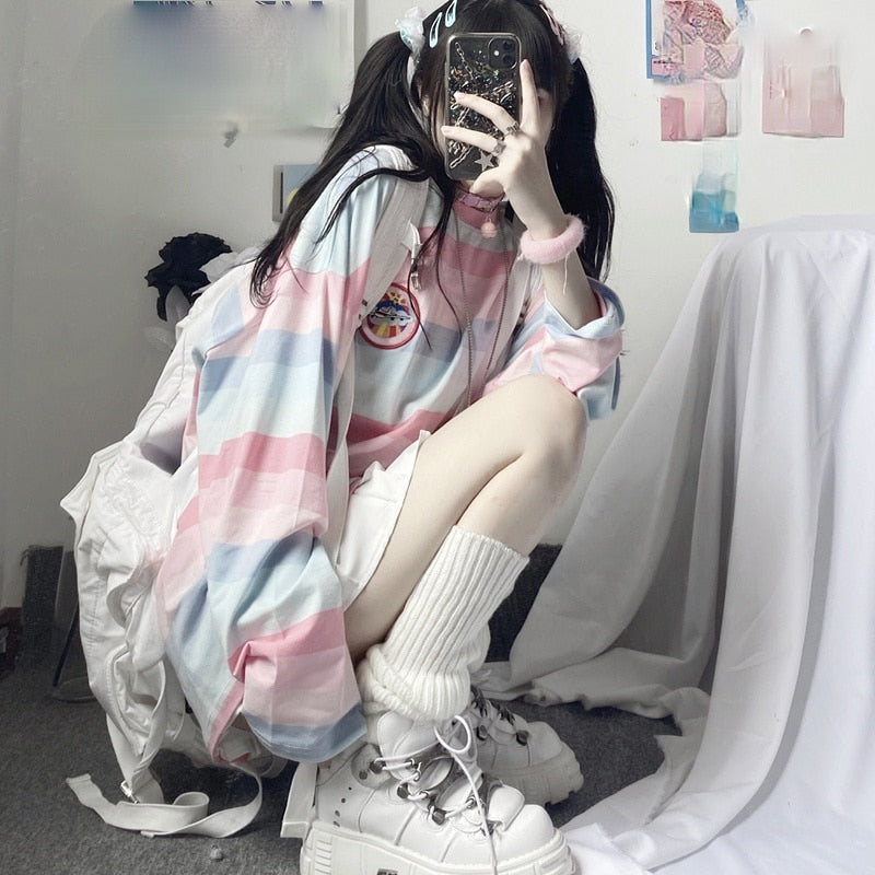 Medium shot with a side view of a model sitting in a pastel-colored Femzai striped shirt, showing off chunky white platform shoes and the shirt's design against a minimalist room background, perfect for soft girl aesthetic outfits.