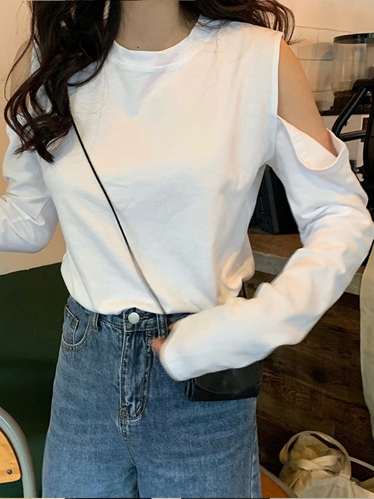 Medium shot side view of a model in a white Femzai cold-shoulder top, complemented with blue high-waisted jeans and a black side bag, set against a casual indoor setting, epitomizing relaxed elegance.