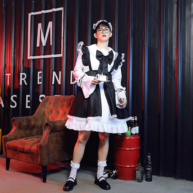 Image Description: Femzai's black and white maid dress product showcased in a medium view. The model, accessorized with glasses and a matching maid headband, stands confidently beside a brown vintage chair holding a white tray. The vibrant background features a vertical "M" sign and red curtains with "TREND CASES". Beverage bottles are artfully placed on the floor beside a red barrel.