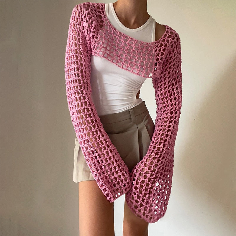 Front view product shot showcasing a vibrant pink crocheted Femzai long-sleeve overlay with intricate design, paired with a fitted white shirt and beige shorts, emphasizing the unique femboy clothing style.