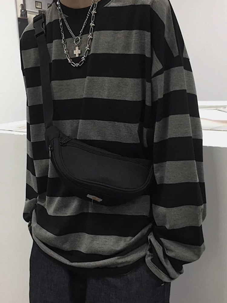 Femzai: Close-up view of a person wearing a black and grey striped sweater, layered silver chain necklace with a cross pendant, and a black waist bag.