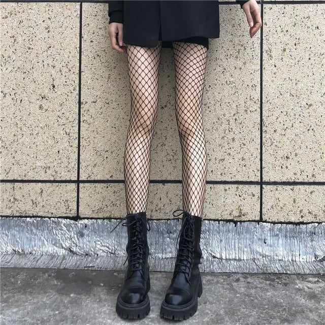 Showcasing a frontal leg view of Femzai's one-size fishnet pantyhose in a striking black large mesh, perfect for making a bold statement in your femboy clothing.