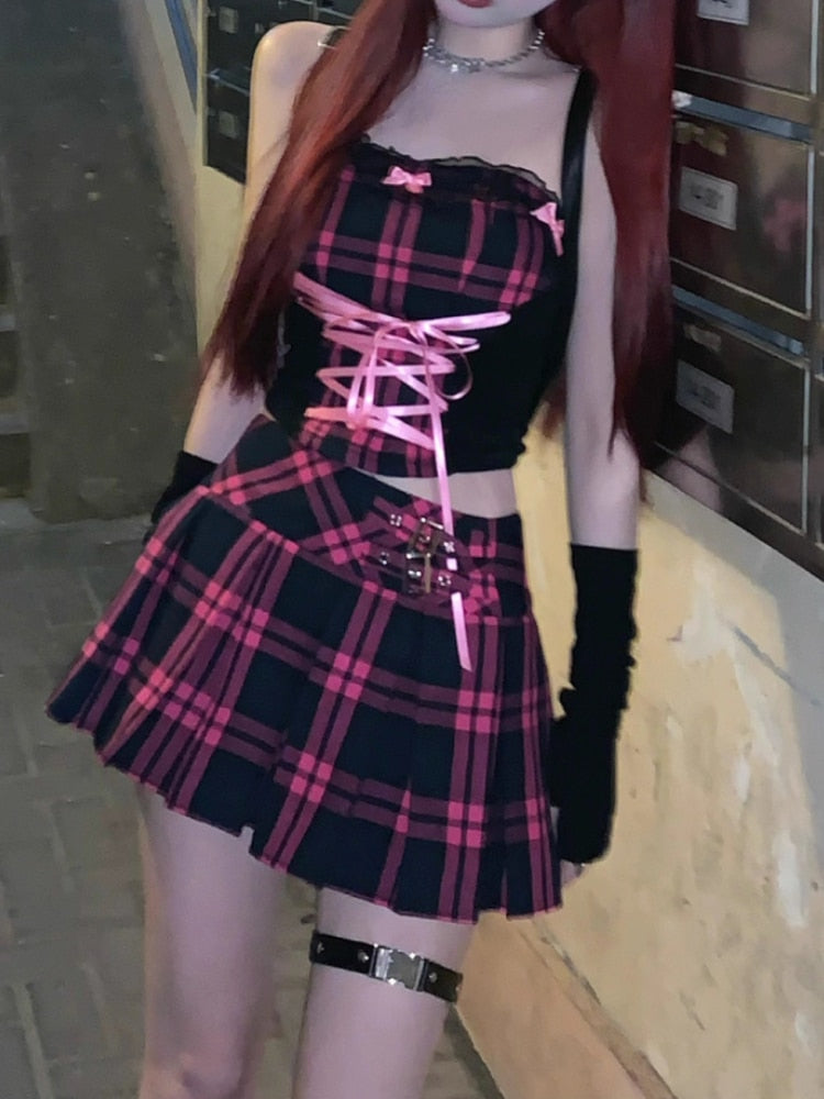 A frontal shot of the same femboy, gracefully standing with arms aloft, emphasizing the lace-up details of their black and pink plaid top. The look is complemented with a matching mini skirt and edgy black thigh bands, encapsulating the iconic femboy style.