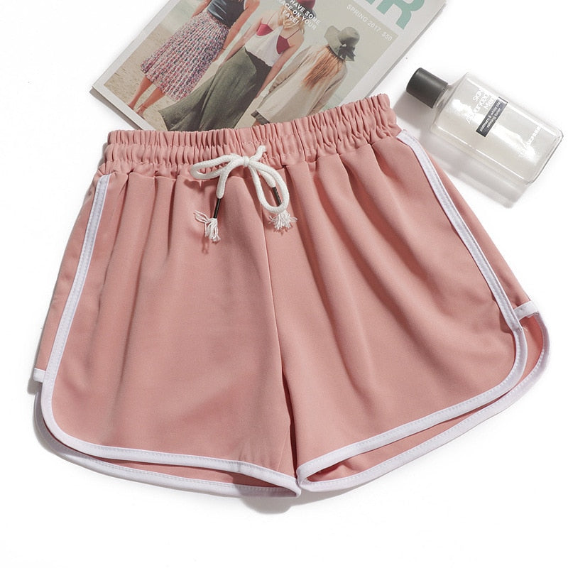 Detail shot of pastel pink dolphin shorts with white accents, displayed with a fashion magazine and fragrance bottle, showcasing the delicate drawstring with tassel ends. A feminine touch to femboy clothing collections
